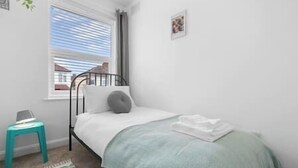 A bedroom with a bed, a window, a small stool, and a picture on the wall. - NEC Birmingham Airport Modern Village Retreat, Sleeps 7, Free Parking (Hampton in Arden)