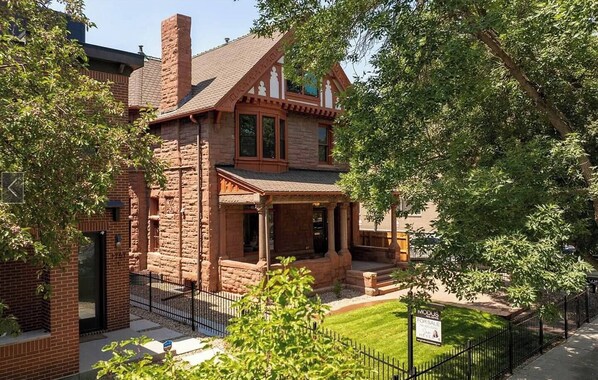A two-story brick house with a porch, a chimney, and a small front yard. - Lioness Downtown Den (Denver)