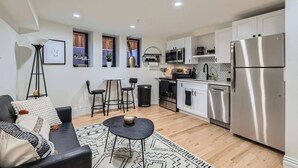 A compact kitchen with modern appliances, a dining area with a sofa and chairs, and a small side table. - Lioness Downtown Den (Denver)