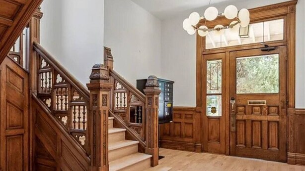 A grand wooden staircase with a chandelier, leading to a room with a large wooden door and windows. - Lioness Downtown Den (Denver)