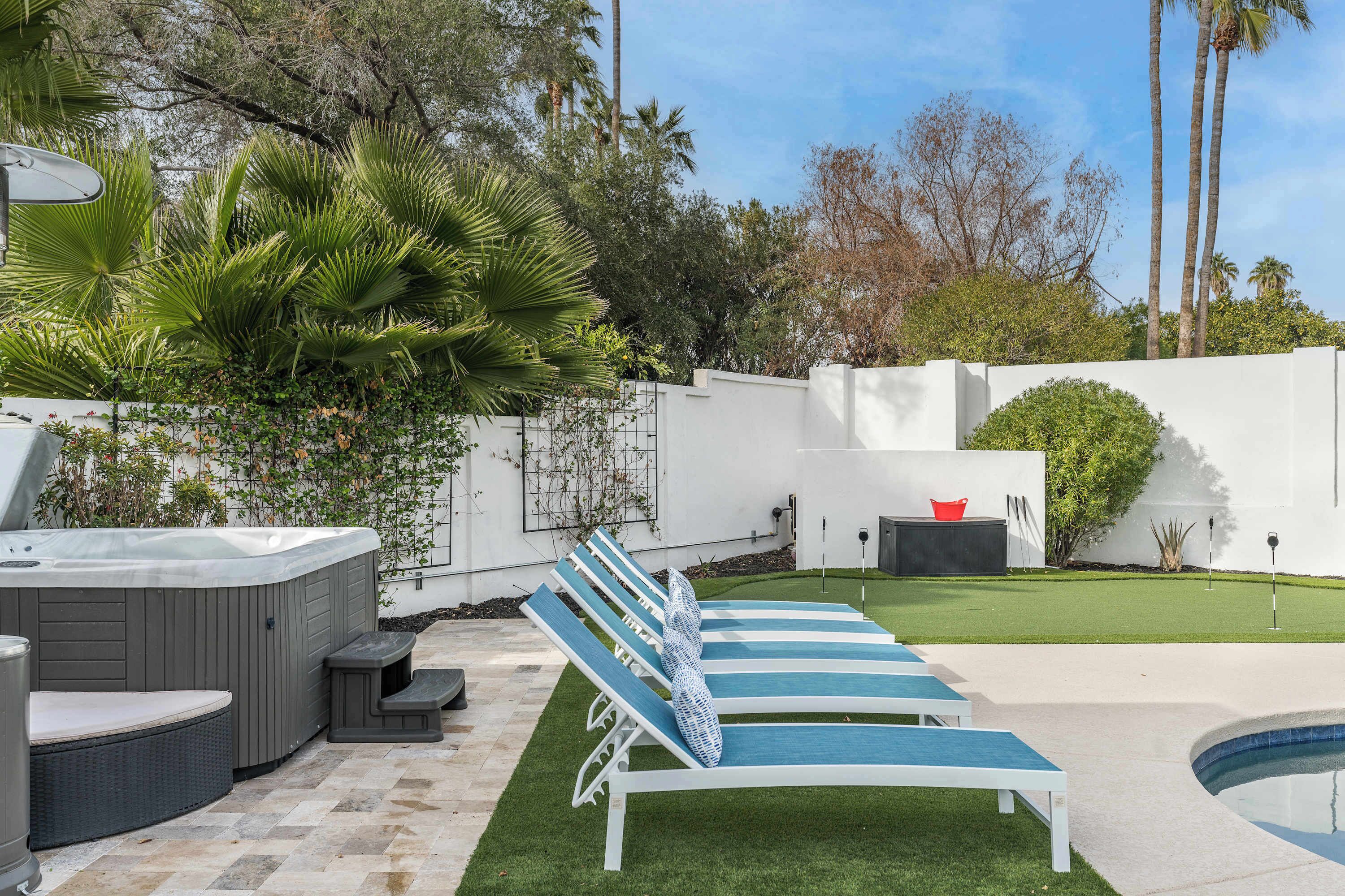 Un jardin avec un jacuzzi, des chaises longues, une petite piscine et une pelouse bien entretenue.