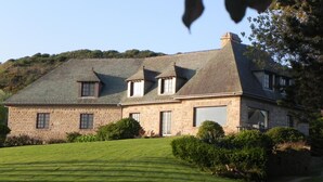 A large stone house with a sloped roof, multiple windows, and a well-maintained lawn. - Spacious house with sea view, fireplace and garden (La Hague)