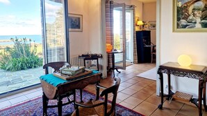 A cozy living room with a view of the sea, a dining area with a table and chairs, and a painting on the wall. - Spacious house with sea view, fireplace and garden (La Hague)