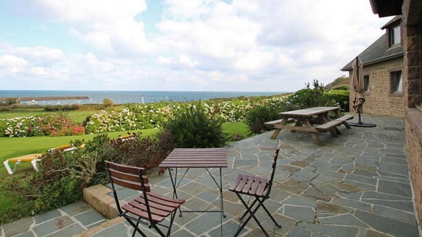 A patio with stone flooring, a wooden table, and two chairs. - Spacious house with sea view, fireplace and garden (La Hague)