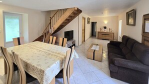 A spacious living area with a dining table, a sofa, a TV, and a staircase.