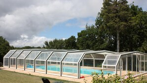 A large greenhouse structure with a pool inside, surrounded by a grassy area and trees.