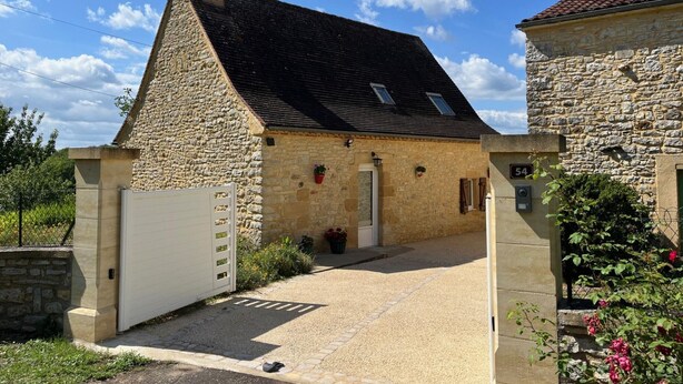 A stone house with a sloped roof, a gated entrance, and a small porch area.