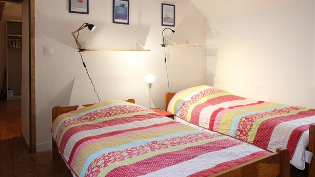 Un dormitorio con dos camas, vigas de madera, techo inclinado y un armario con ropa colgada.