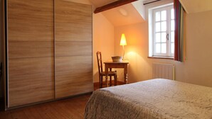 Ein Schlafzimmer mit einem Holzschrank, einem kleinen Tisch mit Lampe und einem Fenster mit Vorhängen.