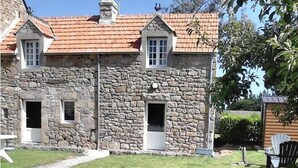 Ein Steinhaus mit rotem Ziegeldach, zwei Fenstern und einer Tür.