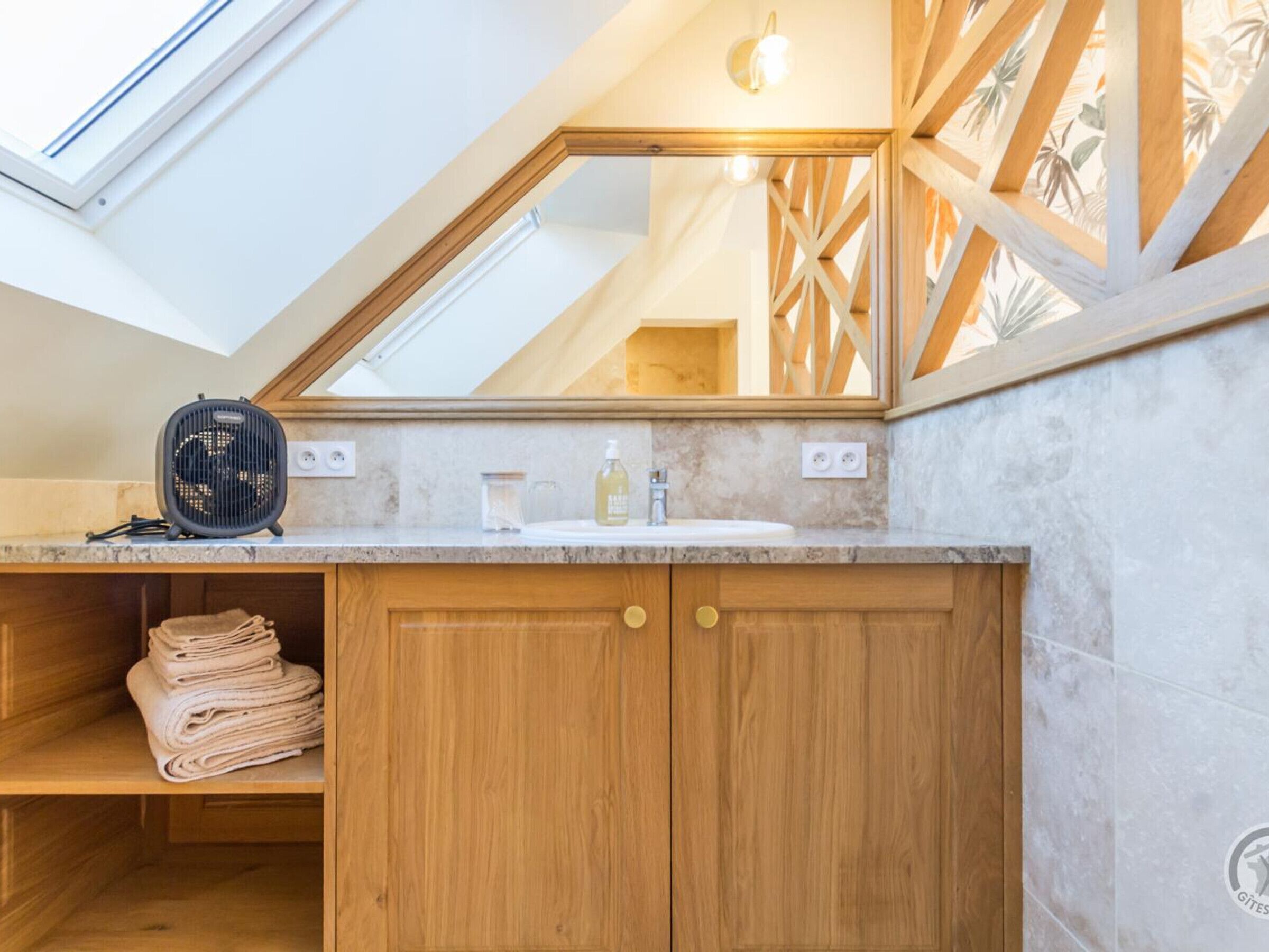Un baño con tragaluz, armarios de madera, un lavabo y un ventilador.