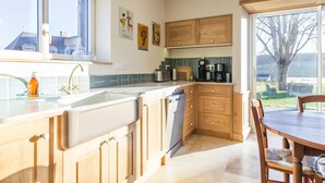 A kitchen with wooden cabinets, a dishwasher, a sink, and a dining area with a table and chairs. - Charming countryside house with large green area (Marcilly)