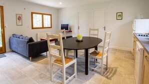 A dining area with a round table, four chairs, a television, and a kitchen area with a refrigerator.