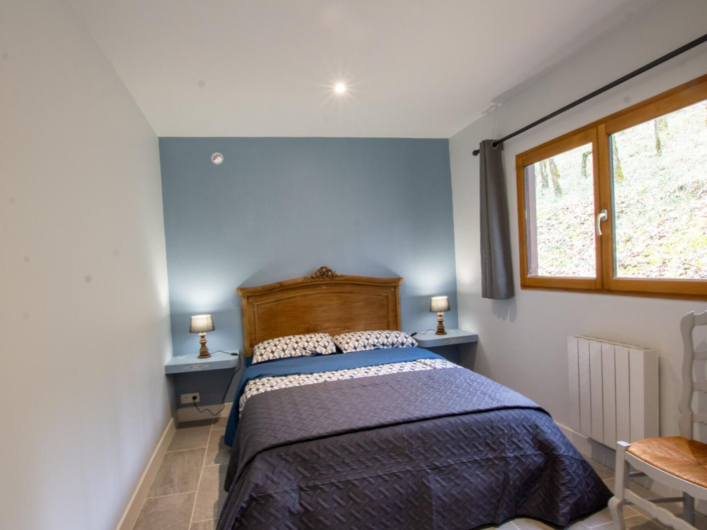 A bedroom with a bed, two bedside tables with lamps, a radiator, a window with curtains, and a chair.