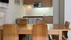 A compact kitchen with wooden cabinets, a microwave, a dishwasher, and a dining table with chairs.
