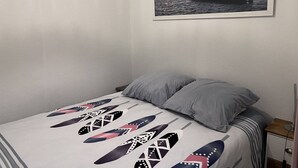 A bedroom with a bed, pillows, a nightstand, a framed picture of a sunset over water, and a wall with a textured finish.
