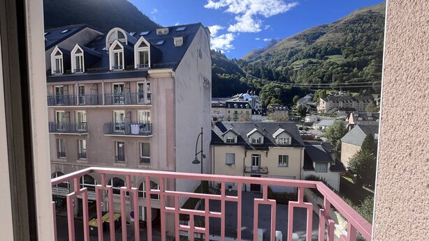 A balcony with a pink railing overlooking a town with buildings and a mountain in the background.