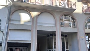 A multi-story building with a central entrance, large arched windows, and a gated driveway.