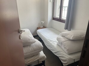A small, single-bed room with a window, a bedside table, and a lamp.