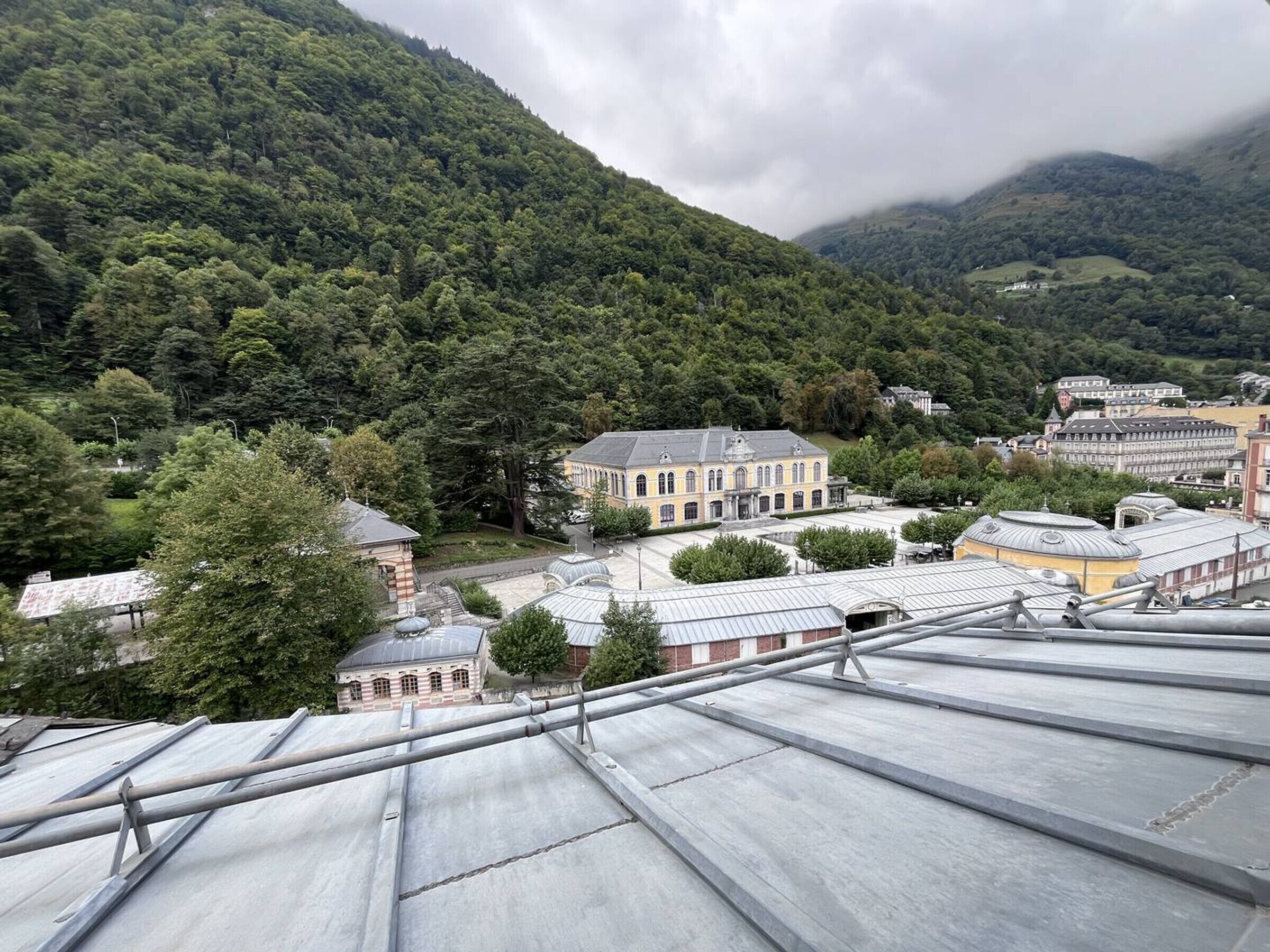 A view of a building with a large central courtyard surrounded by trees and a mountain in the background.
