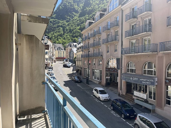 Straßenansicht mit Gebäuden, Autos und einem Balkon.