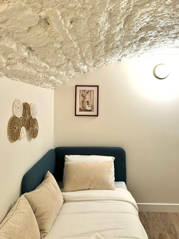 A bedroom with a blue headboard, a bed with white bedding, a framed picture on the wall, and a textured ceiling. - Apartment Saint Germain des Pres Bon Marche (Paris)