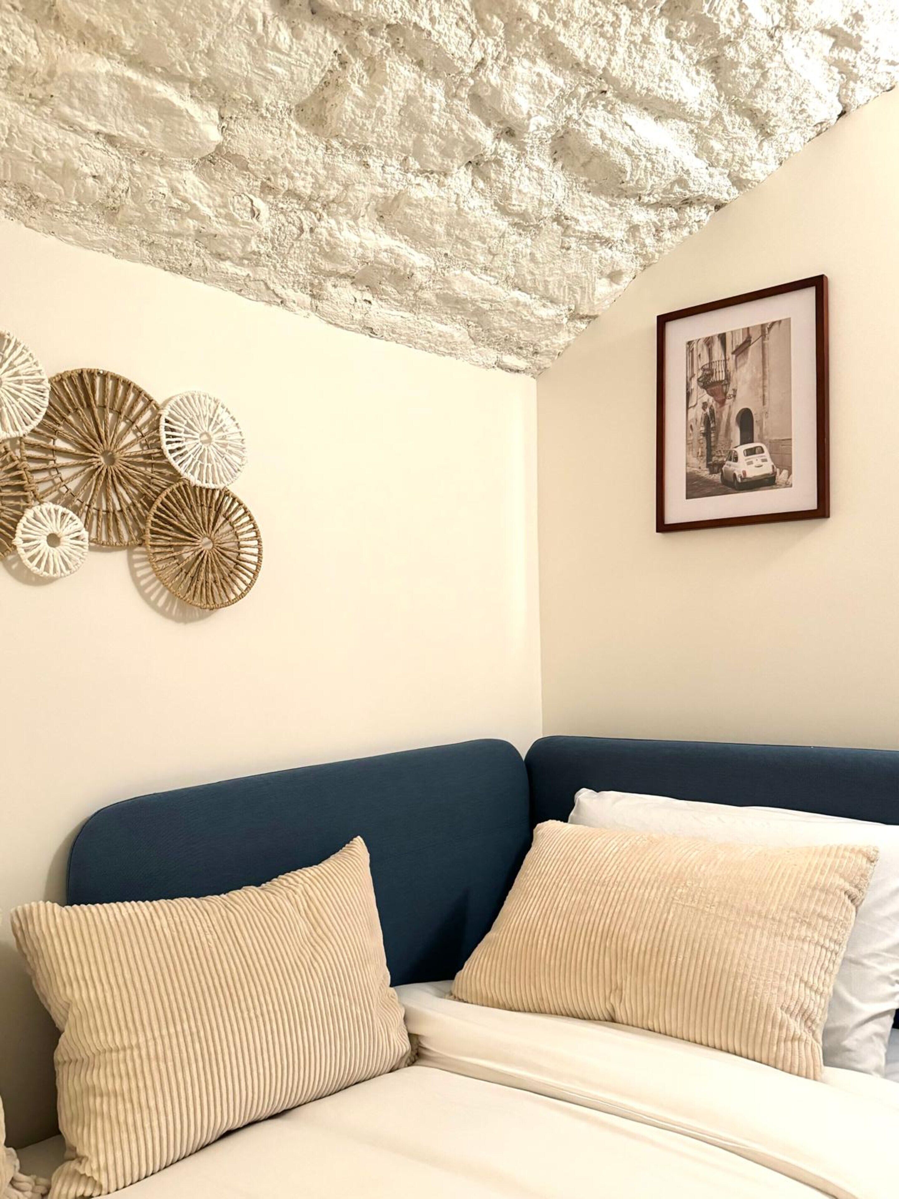 Quarto com um sofá azul, almofadas bege e teto texturizado.