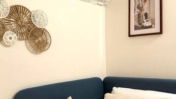 Quarto com um sofá azul, almofadas bege e teto texturizado.