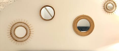 A bedroom with a bed, two round mirrors, and decorative wall art.