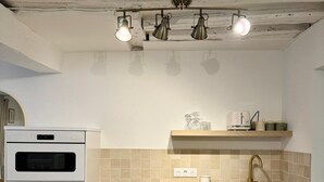A kitchen with white cabinets, a wooden countertop, a built-in oven, a sink with a gold faucet, and a ceiling with exposed beams and pendant lights. - Apartment Saint Germain des Pres Bon Marche (Paris)