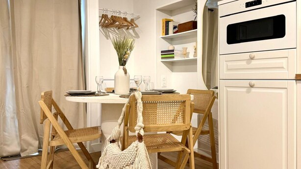 A cozy kitchen with wooden chairs, a white cabinet, and a dining table with a vase and books. - Apartment Saint Germain des Pres Bon Marche (Paris)