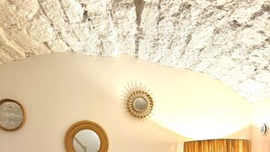 A bedroom with a bed, a round mirror, a sunburst wall decoration, a tall floor lamp, and a small round table with a white vase. - Apartment Saint Germain des Pres Bon Marche (Paris)