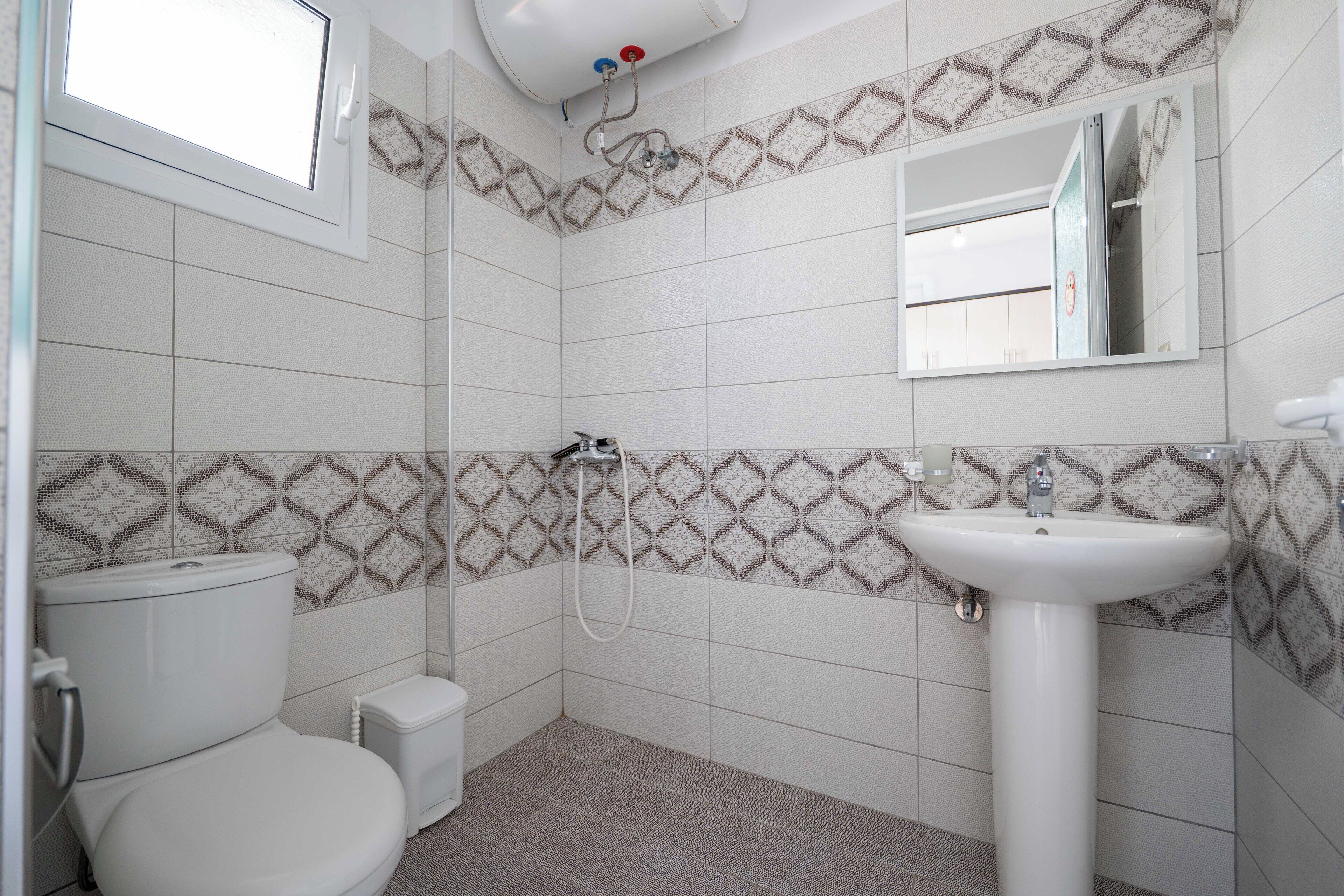 Een badkamer met toilet, wastafel, douche en een raam.