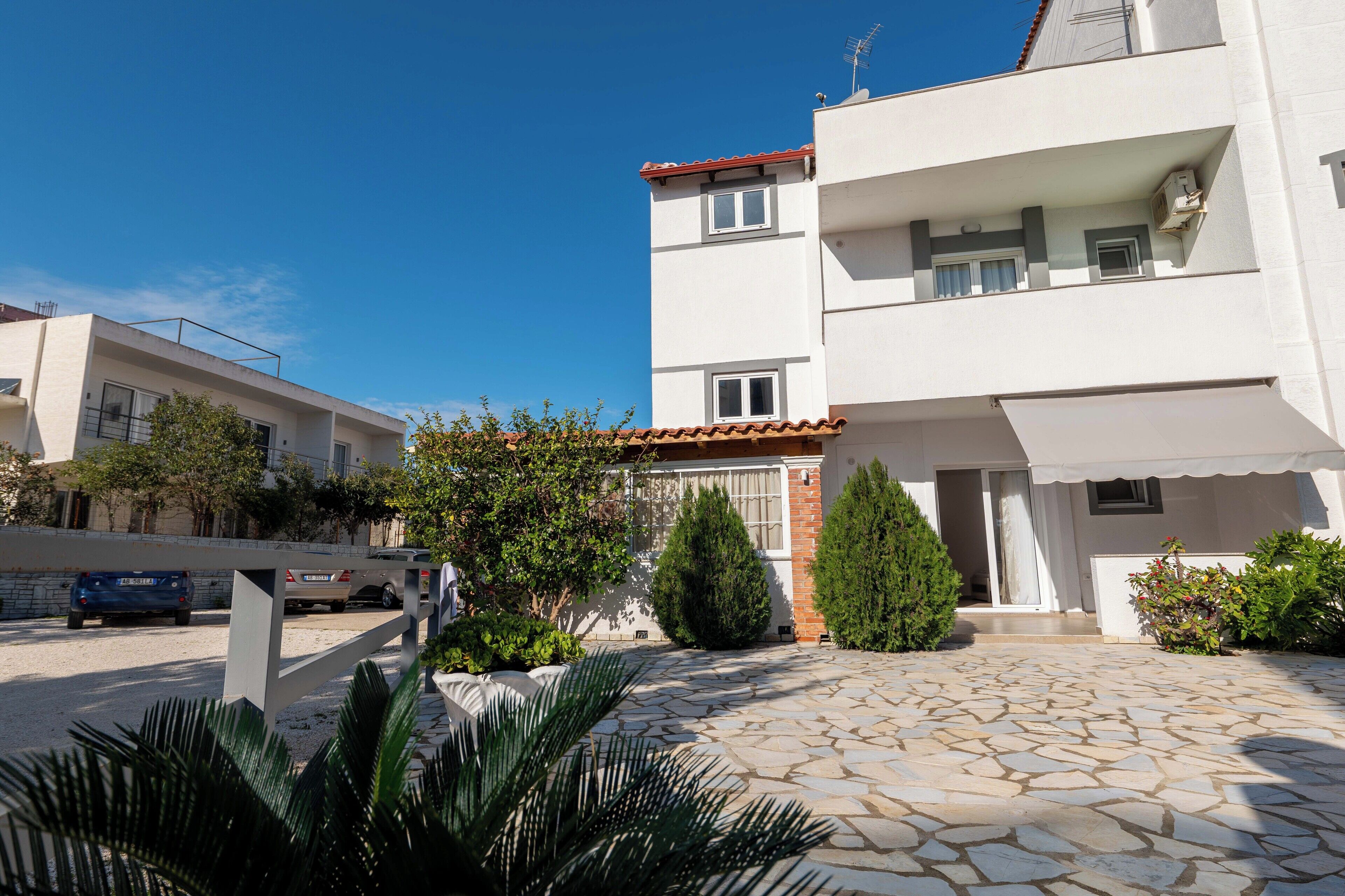 A modern two-story building with a stone-paved courtyard, a balcony, and a car parked in the driveway.