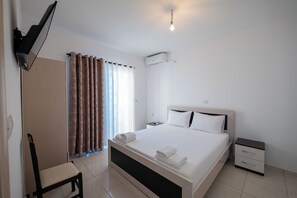 A modern hotel room with a large bed, a bedside table, a chair, and a flat-screen TV mounted on the wall. - Aktea Apartments (Ksamil)