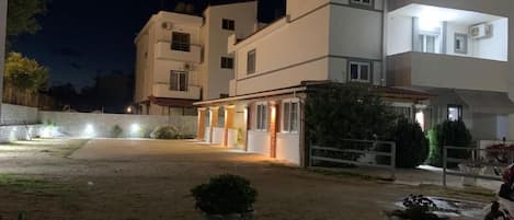 A residential building with multiple floors, a paved driveway, and outdoor lighting.