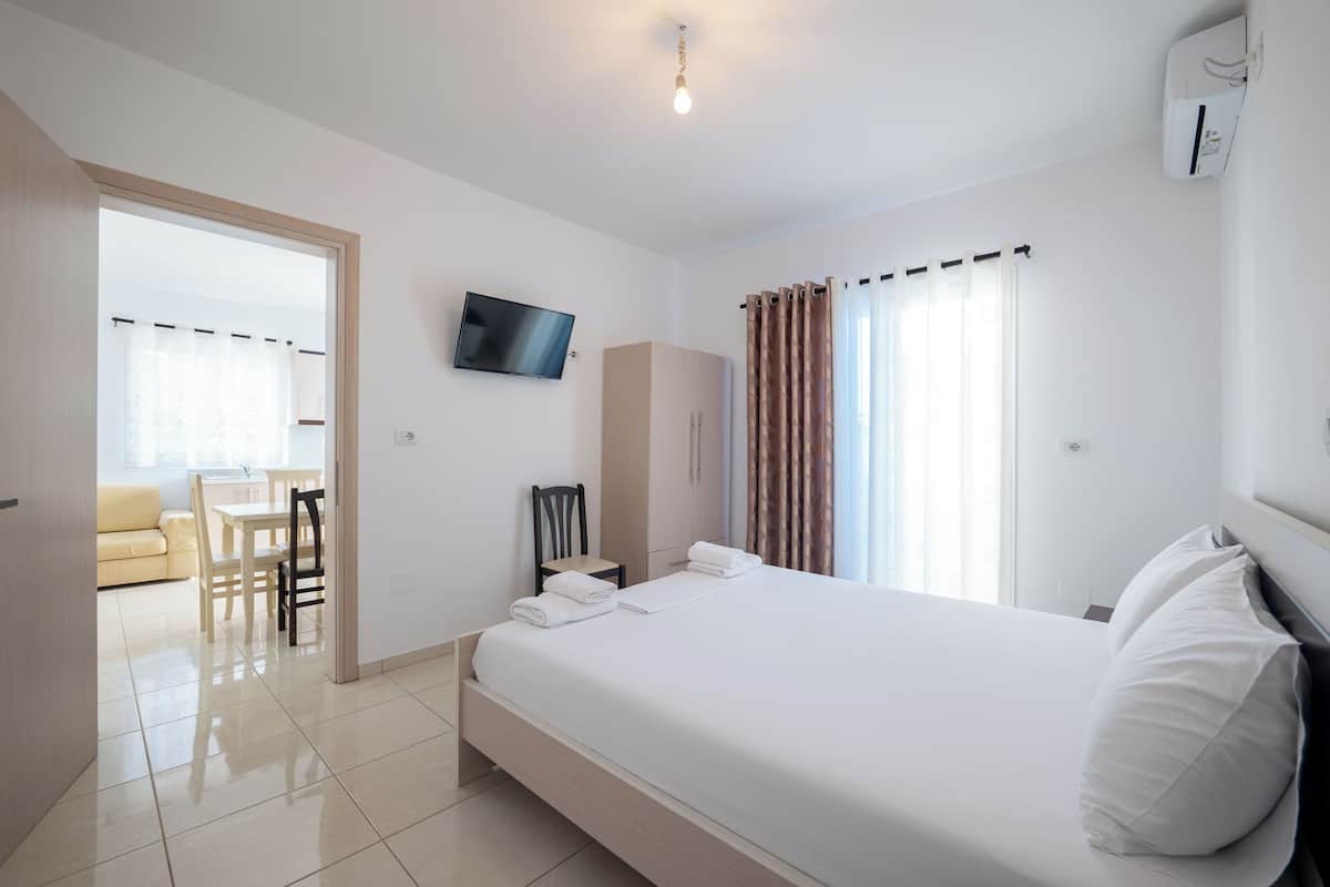 A hotel room with a bed, a TV, a wardrobe, and a dining area with a table and chairs.