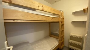 Un lit superposé avec un matelas et un oreiller, une petite étagère et une porte dotée d’une poignée.