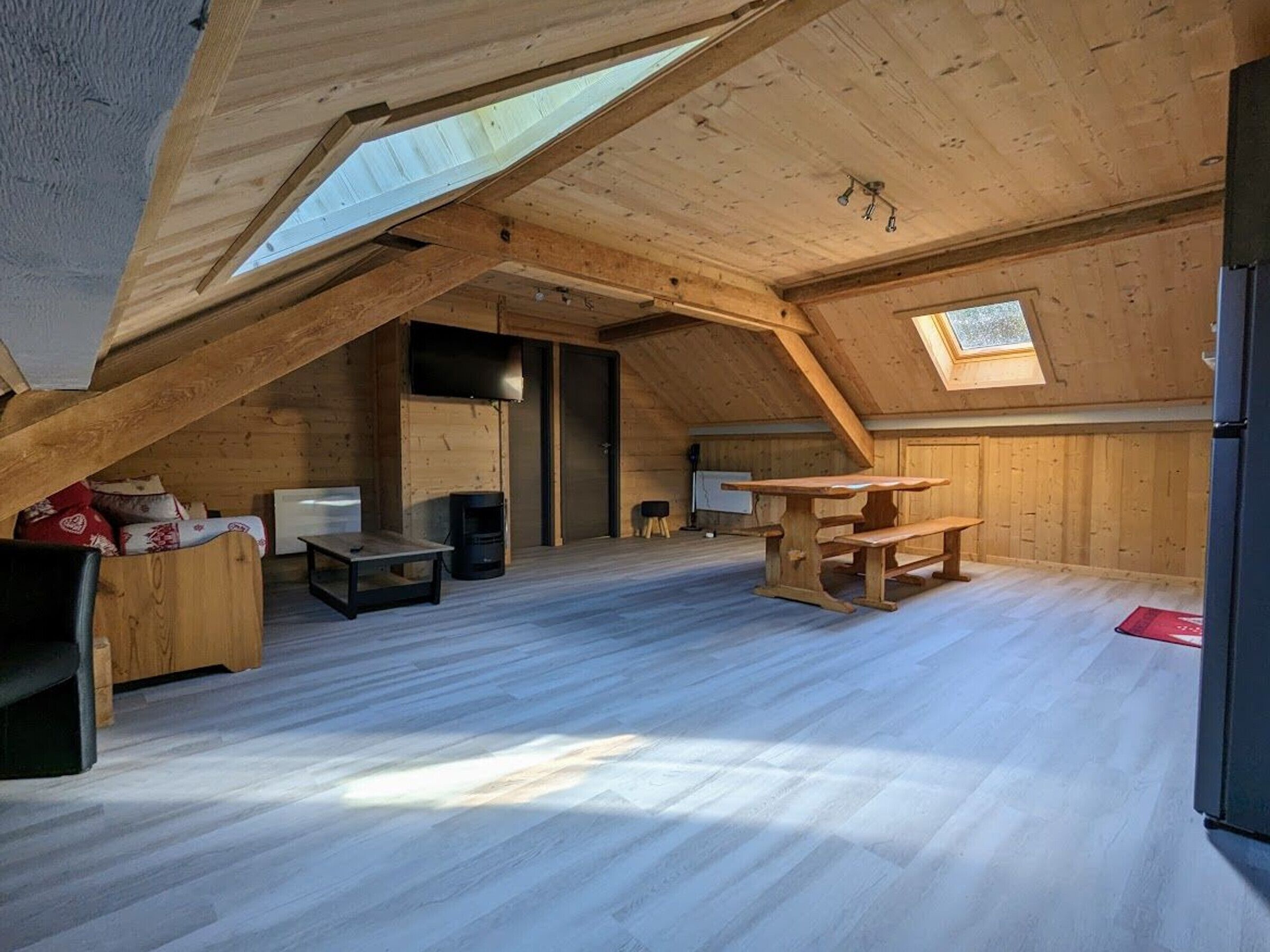 An attic room with wooden beams, a skylight, a wooden table, and a bench.