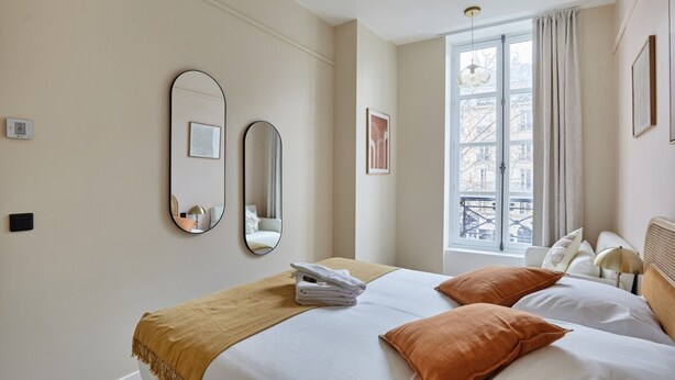 A hotel room with a bed, a window with curtains, a mirror, and a wall-mounted light fixture. - Sublim Apartement in the Center of Paris/le Marais (Paris)