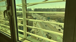Vista desde un piso alto con una ventana que da a una autopista concurrida, con varios carriles de tráfico y edificios a lo lejos.