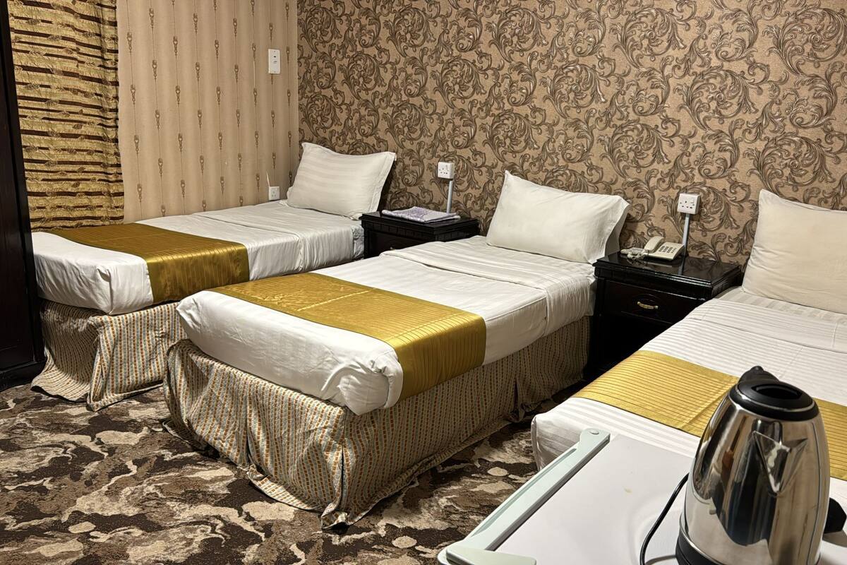A hotel room with two single beds, a double bed, a bedside table with a phone, and a coffee maker.