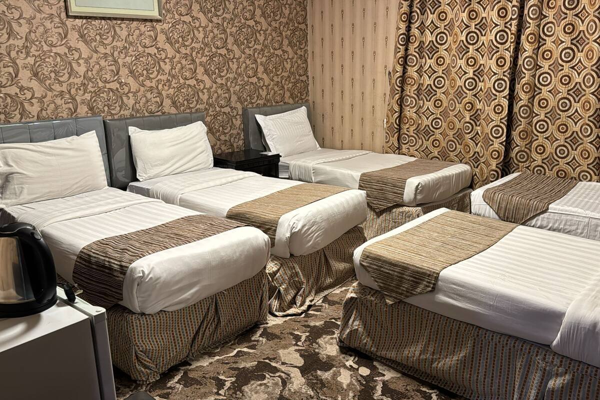 A hotel room with four single beds, a desk with a kettle, patterned curtains, and a carpeted floor.