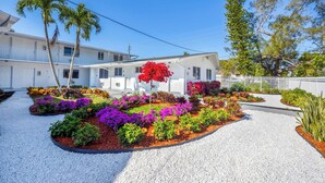 A white two-story building with a gravel driveway and colorful flower beds. - Stylish Miami Studio | Parking+Gym | Near Aventura (Miami)