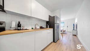 A modern kitchen with white cabinets, a stainless steel refrigerator, and a wooden countertop. - Stylish Miami Studio | Parking+Gym | Near Aventura (Miami)