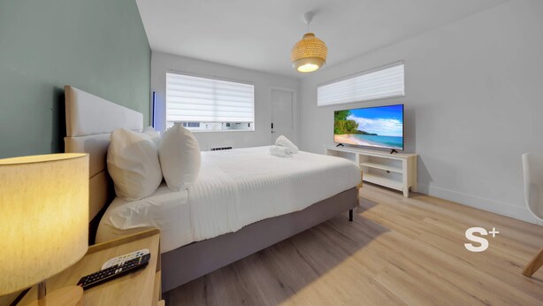 A modern hotel room with a large bed, a TV on a stand, a lamp, and a remote control on a nightstand. - Stylish Miami Studio | Parking+Gym | Near Aventura (Miami)
