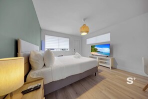 A modern hotel room with a large bed, a TV on a stand, a lamp, and a remote control on a nightstand. - Stylish Miami Studio | Parking+Gym | Near Aventura (Miami)