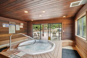 Un espace spa doté d’un jacuzzi, de murs en bois et offrant une vue sur l’espace piscine extérieure.