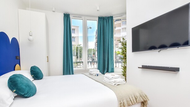 Ein modernes Hotelzimmer mit einem großen Bett, lindgrünen Vorhängen, einem Flachbildfernseher und einem Balkon mit Blick auf die Stadt.