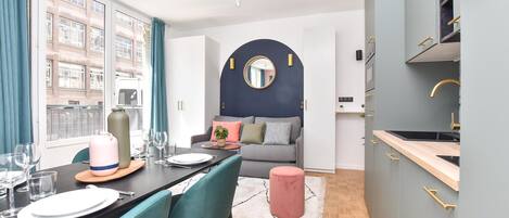 Una cocina moderna con armarios grises, un espejo redondo y una zona de comedor con sillas color turquesa y una mesa de madera.